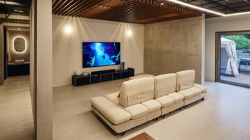 A modern living room with a large flat-screen TV, a beige sectional sofa, and a minimalist design.