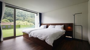 Un dormitorio moderno con una cama grande, vistas a un paisaje verde y una lámpara de pie.