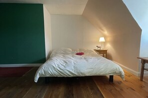 Ein Einzelbett mit weißer Daunendecke in einem Zimmer mit schrägem Dach und einer grünen Akzentwand.
