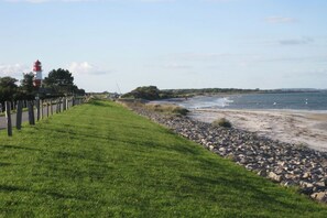 Ein Küstenpfad mit einem Leuchtturm, grünen Wiesen und einer felsigen Küstenlinie.