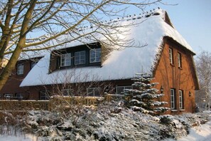A traditional house with a steeply pitched roof covered in snow, surrounded by a snow-covered garden and a tree. - Holiday apartment with 3 bedrooms (Gelting)