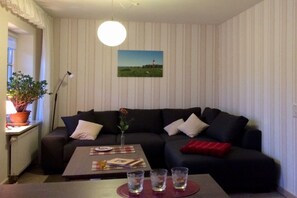 Een woonkamer met een donkergrijze bank, een bijzettafeltje met onderzetter en een potplant.