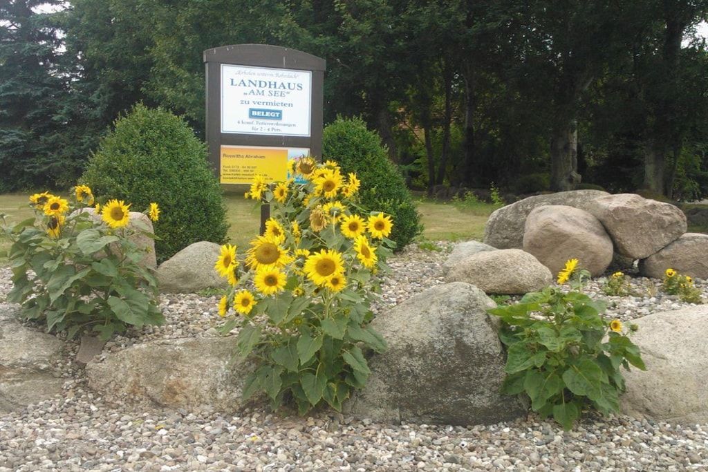 A sign for LANDHAUS AM SEE with a garden of sunflowers and rocks.