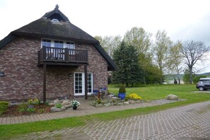 Ein Ziegelhaus mit Balkon, ein Garten mit Blumen und Rasen sowie ein geparktes Auto in der Nähe.
