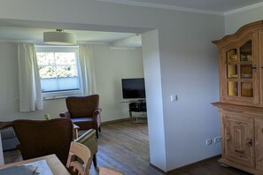 Ein Wohnzimmer mit Fernseher, einer Holzkommode und einem Essbereich mit Stühlen.