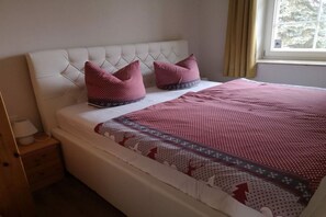 Ein Schlafzimmer mit einer gesteppten Kopfteil, einem Bett mit gemustertem Bettbezug, zwei Kissen, einem Nachttisch mit einer Lampe und einem Fenster mit Vorhängen.