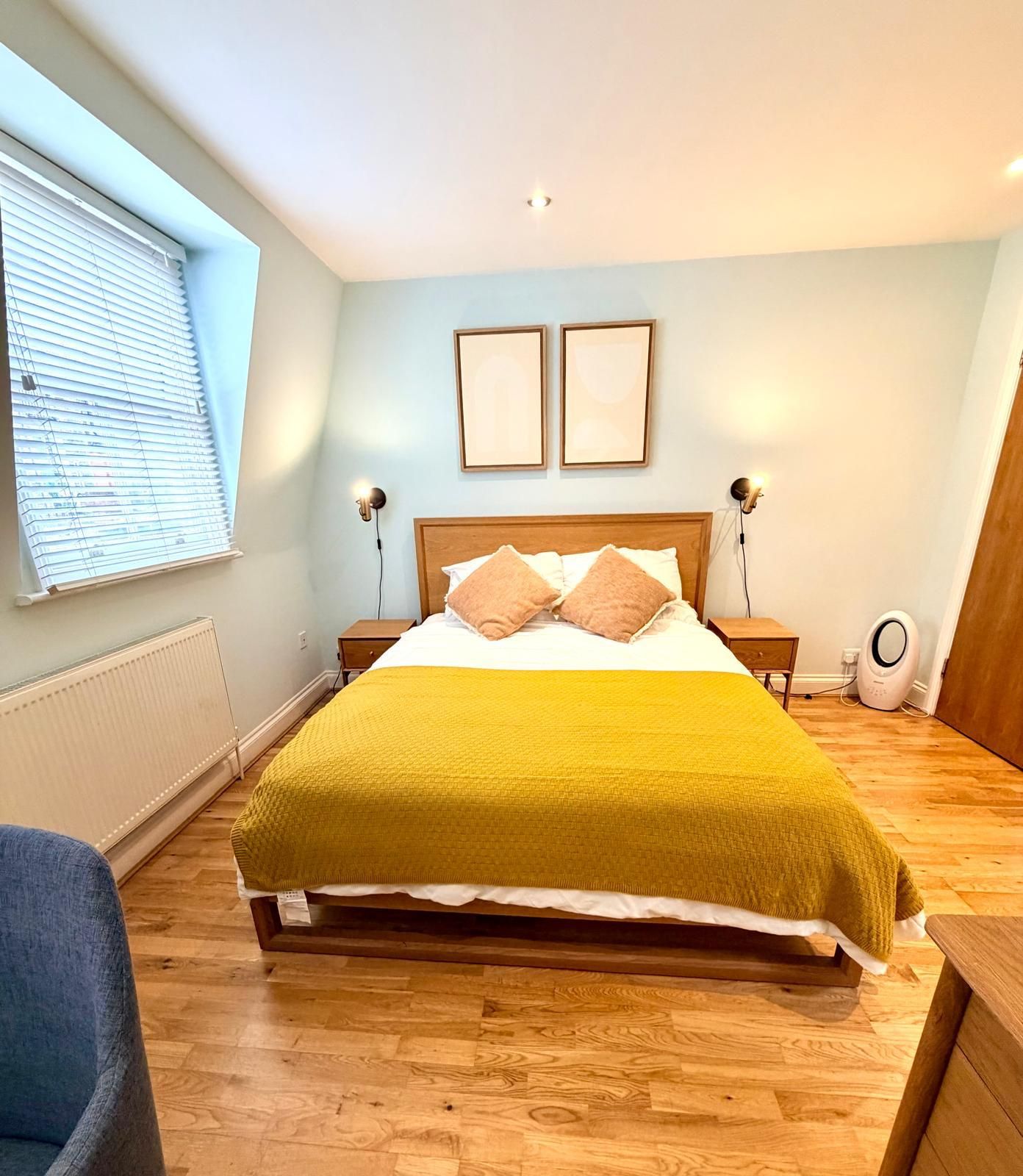 Une chambre à coucher comprenant un lit, deux lampes de chevet, un radiateur, une fenêtre avec des stores et une porte.