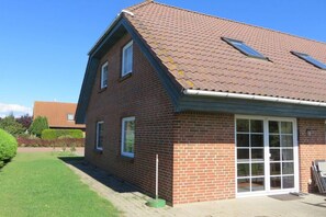A two-story brick house with a tiled roof, a sliding glass door, and a small garden area. - Island apartment Fehmarn (Puttgarden\/Fehmarn)