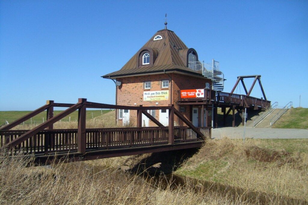 A brick building with a metal roof, a wooden bridge, and a staircase leading to a platform.