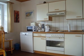 A compact kitchen with white appliances, a microwave, a coffee maker, and a dishwasher. - Island apartment Fehmarn (Puttgarden\/Fehmarn)