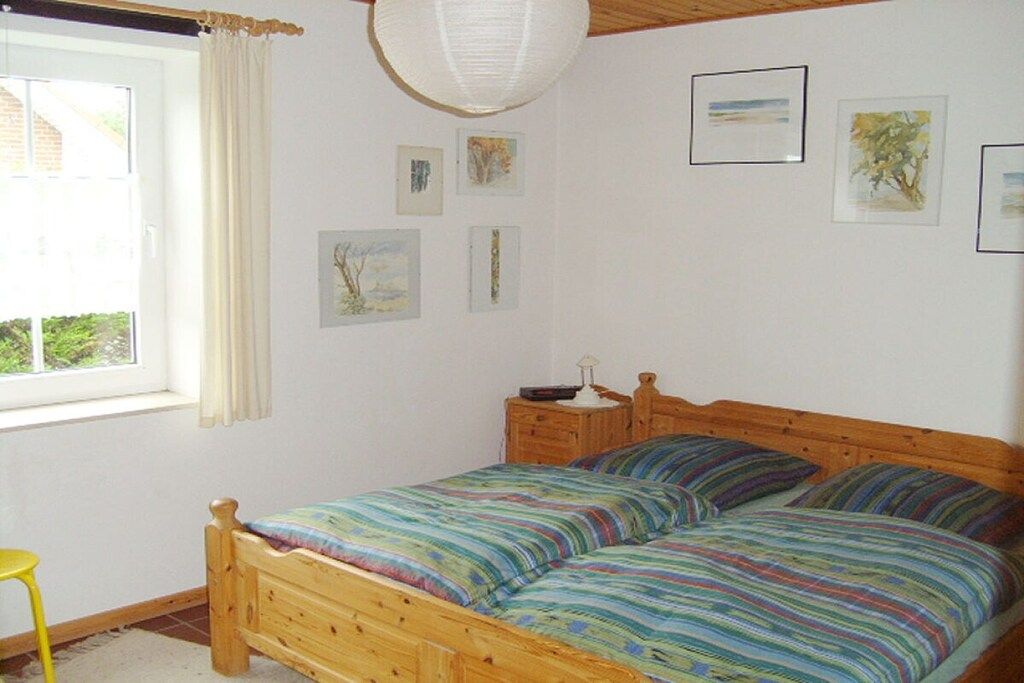A bedroom with a wooden bed, a nightstand, a window with curtains, and wall art.