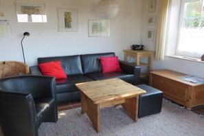A living room with a black leather sofa, a wooden coffee table, a black armchair, and a wooden side table. - Island apartment Fehmarn (Puttgarden\/Fehmarn)