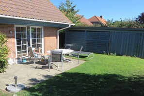 A backyard with a patio, a brick house, a metal fence, and a lawn. - Island apartment Fehmarn (Puttgarden\/Fehmarn)