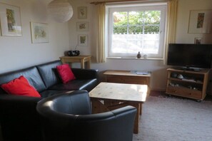 A living room with a sofa, a coffee table, a television, and a window with curtains. - Island apartment Fehmarn (Puttgarden\/Fehmarn)