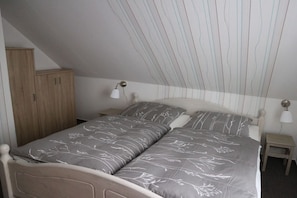 A bedroom with a bed, nightstands, a wardrobe, and a sloped ceiling. - Holiday home in Ludorf with swimming pool (Ludorf)