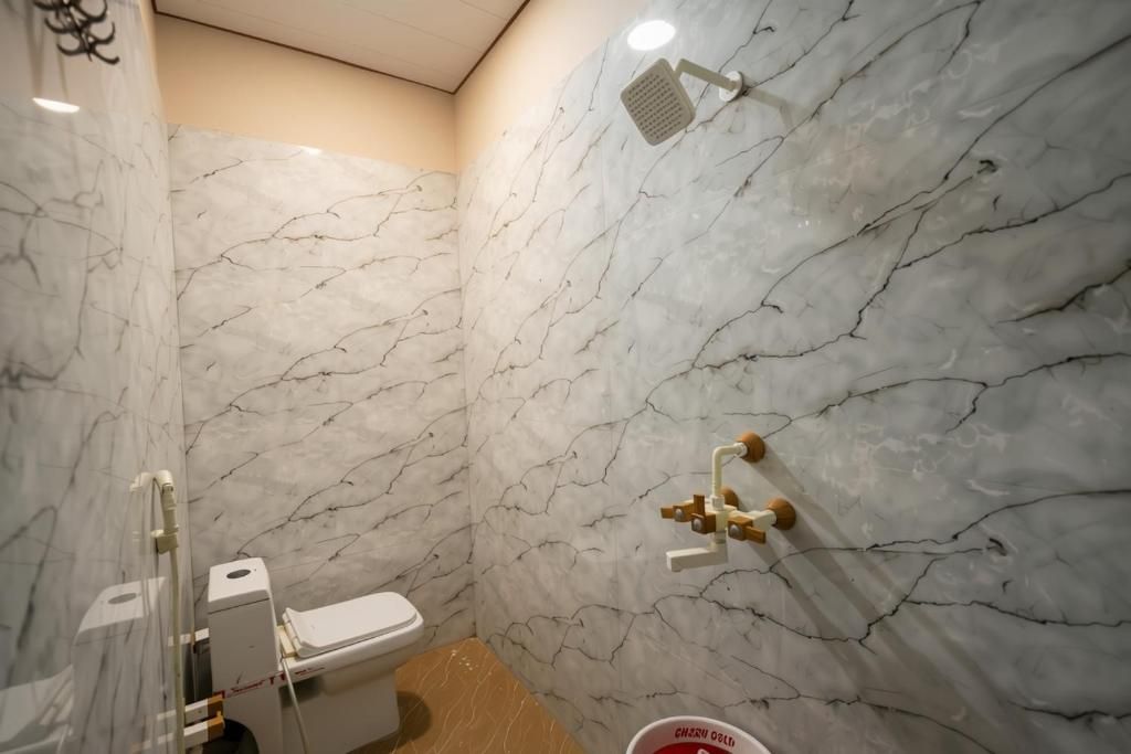 Un baño con inodoro, ducha y paredes de mármol.