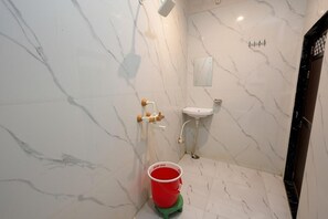 Un baño con pared de mármol, un lavabo, una ducha y un cubo rojo sobre un taburete verde.