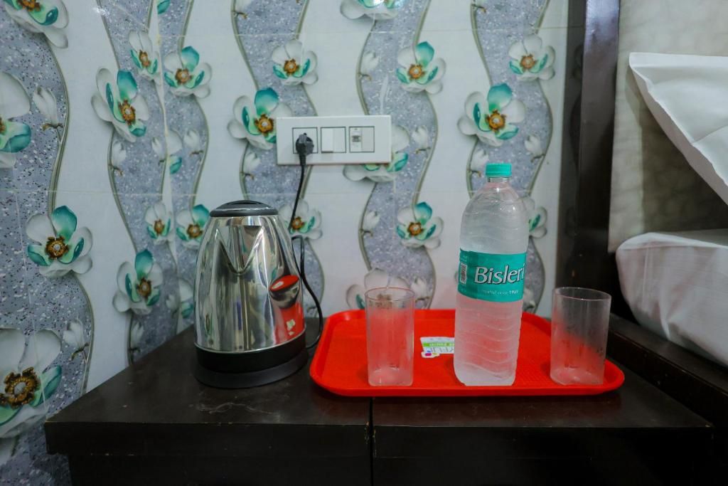 Uma cozinha compacta com chaleira, uma garrafa de água Bisleri e dois copos em um jogo de bandeja vermelho.