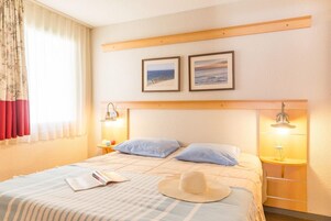 Habitación de hotel con una cama, dos cuadros en la pared, una mesita de noche con una lámpara y una ventana con cortinas.
