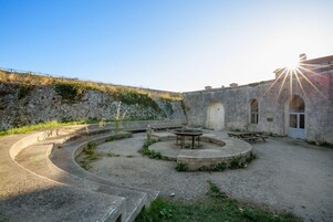 Un patio con una zona de estar circular, una mesa de picnic y un edificio con ventanas de arco.