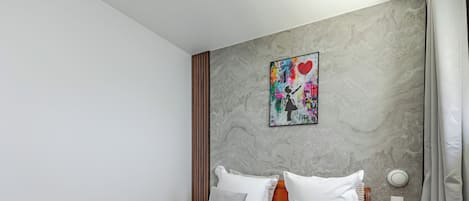Une chambre d’hôtel avec un lit, des oreillers, une tête de lit, une table de chevet, un tableau accroché au mur et un rideau.