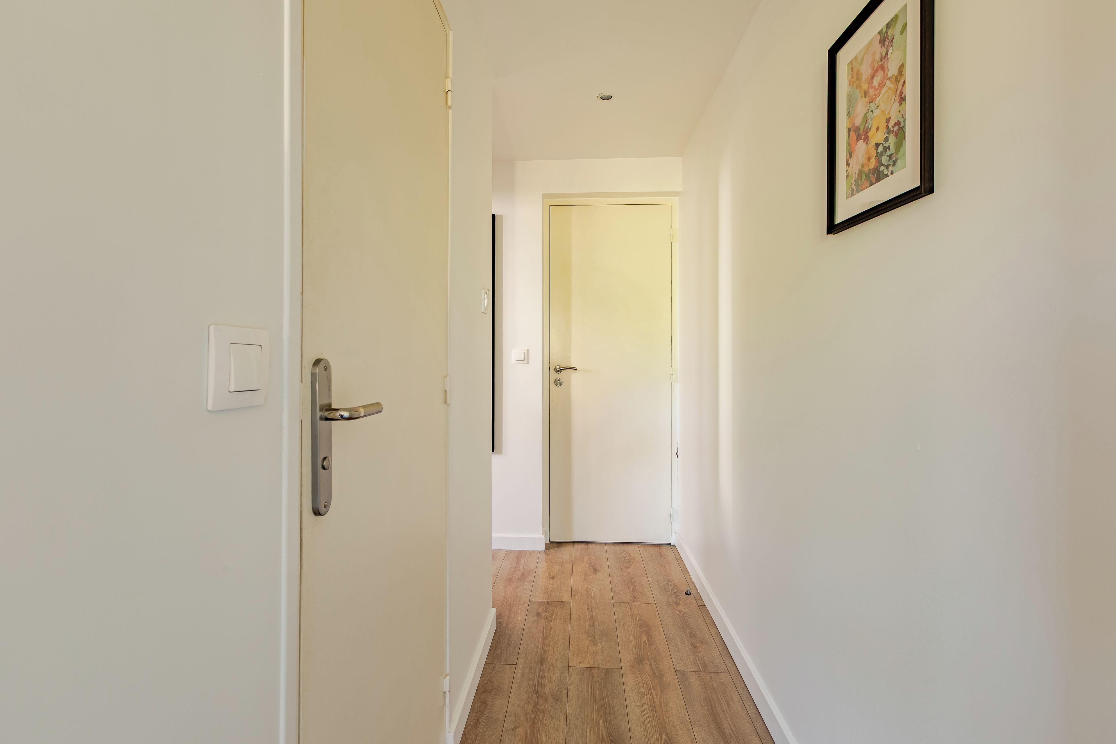Un couloir avec un plancher en bois, des murs blancs et une porte au fond.