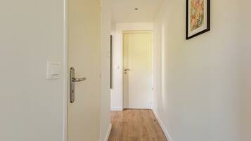 Un couloir avec un plancher en bois, des murs blancs et une porte au fond.
