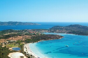Paesaggio costiero con spiaggia, acque blu cristalline e imbarcazioni.