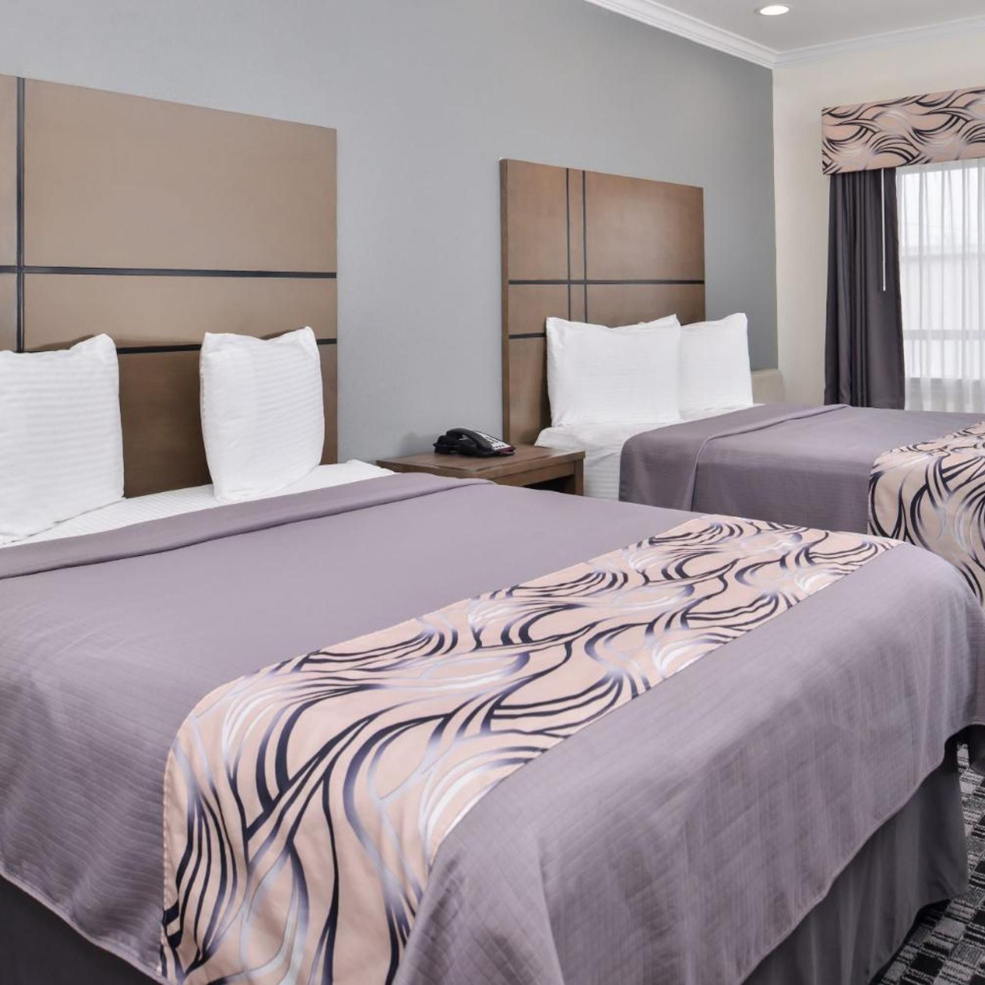 A hotel room with two beds, each with a headboard, a bedside table with a phone, and a window with curtains.