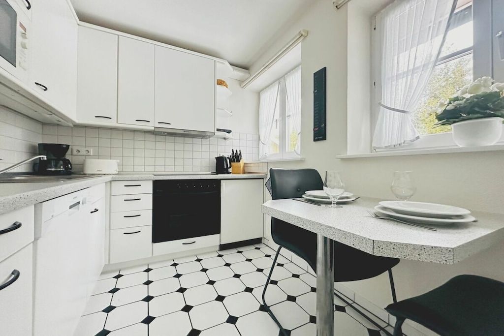 A modern kitchen with white cabinets, a black dishwasher, and a dining area with a table and chairs.