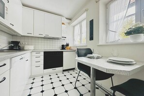 Eine moderne Küche mit weißen Schränken, einem schwarzen Geschirrspüler und einem Essbereich mit Tisch und Stühlen.