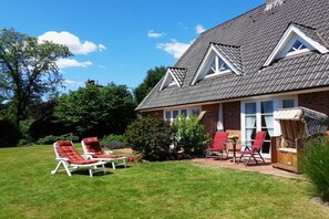 Ein Haus mit geneigtem Dach, einer Ziegelaußenwand und einem gepflegten Rasen mit roten Liegestühlen.