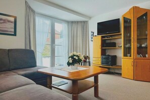 A living room with a sofa, a coffee table, a television, and a cabinet with glass doors. - Holiday home with 1 bedroom (St. Peter - Ording)