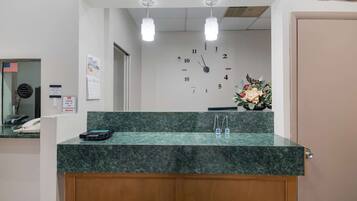 A reception desk with a clock, a phone, and a vase of flowers.