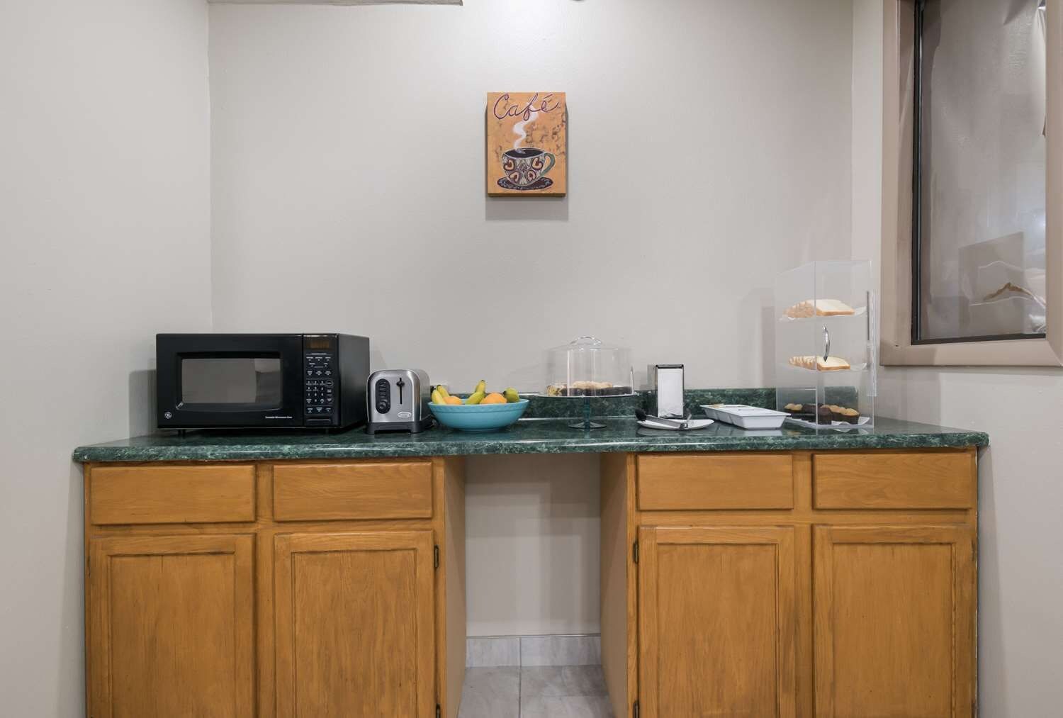 A kitchenette with a microwave, toaster, and a bowl of fruit on the counter.