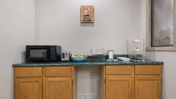 A kitchenette with a microwave, toaster, and a bowl of fruit on the counter.