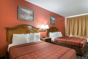 A hotel room with two beds, a nightstand, a lamp, and two framed pictures on the wall. - Rodeway Inn Wormleysburg - Harrisburg (Lemoyne)