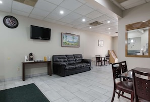 A living room with a black leather sofa, a coffee station, a flat-screen TV, a framed landscape painting, and a dining area with chairs and a table. - Rodeway Inn Wormleysburg - Harrisburg (Lemoyne)