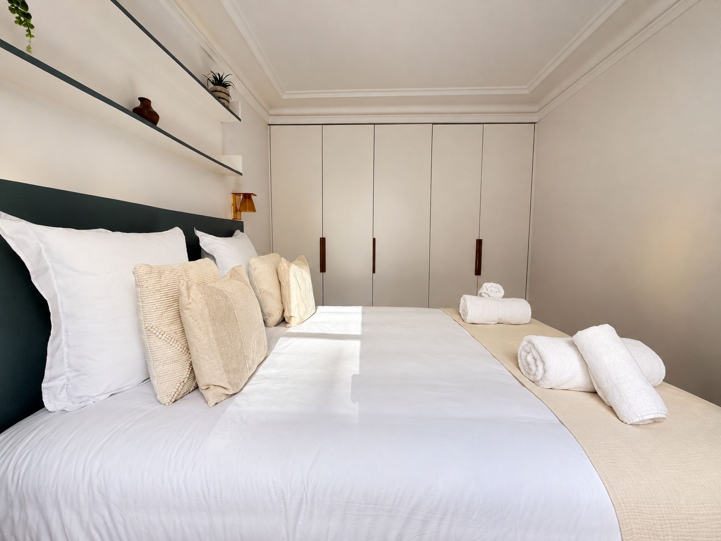 Una habitación de hotel con una cama, almohadas, una mesita de noche, una lámpara y un armario.