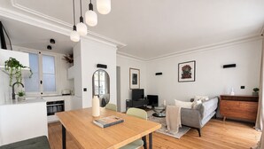 Un apartament modern amb zona de menjador, cuina, saló i un sofà gris.