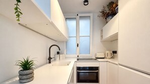 Una cuina moderna amb armaris blancs, forn integrat, rentaplat i finestra amb vidre translúcid.