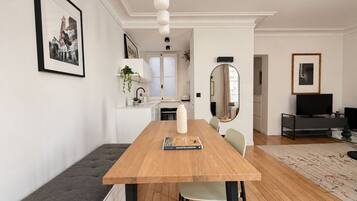 A modern living space with a wooden dining table, a bench, a kitchen area, and a television in the corner.