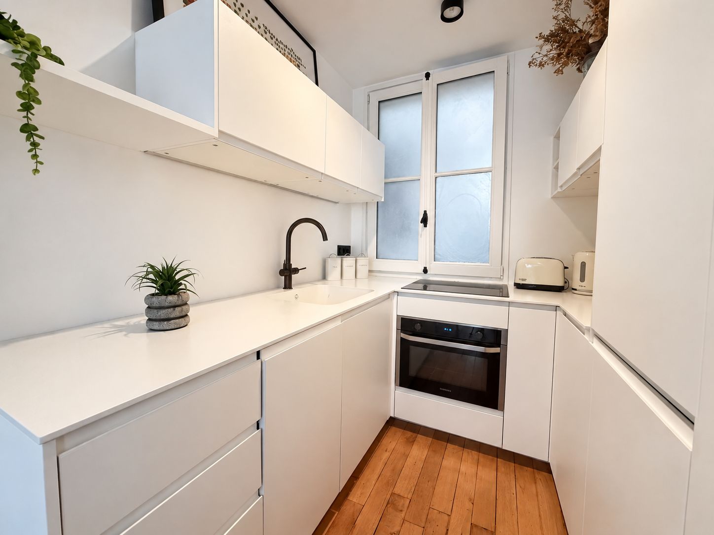 A modern kitchen with white cabinetry, a built-in oven, and a window with frosted glass.