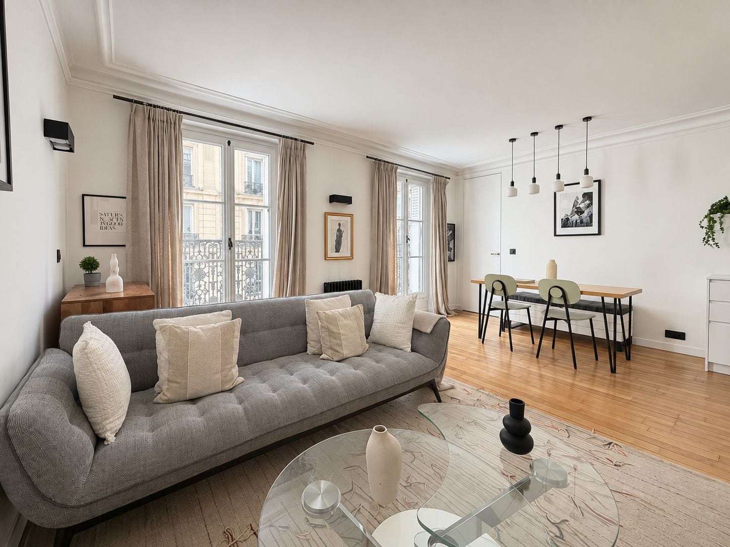 A modern living room with a grey sofa, a glass coffee table, and a dining area with a table and chairs.