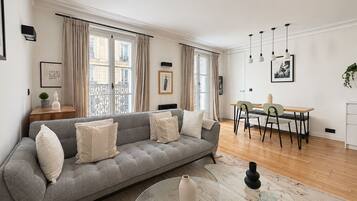 A modern living room with a grey sofa, a glass coffee table, and a dining area with a table and chairs.