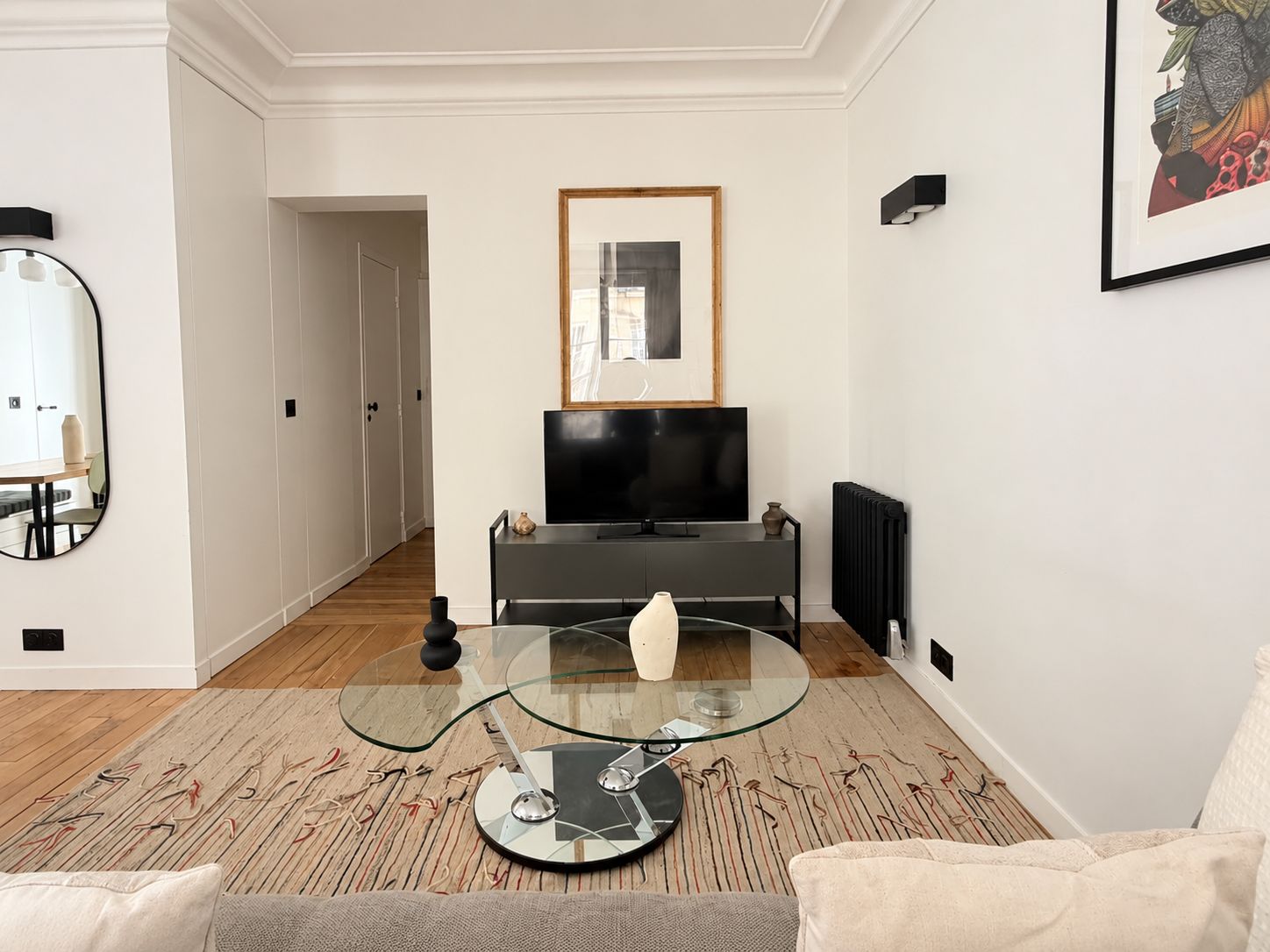 A modern living room with a glass coffee table, a flat-screen TV on a black stand, and a framed picture on the wall.