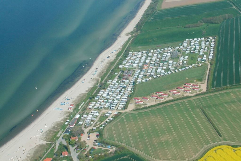 Vue aérienne d’une zone côtière avec une rangée de maisons mobiles, une plage et des champs agricoles.
