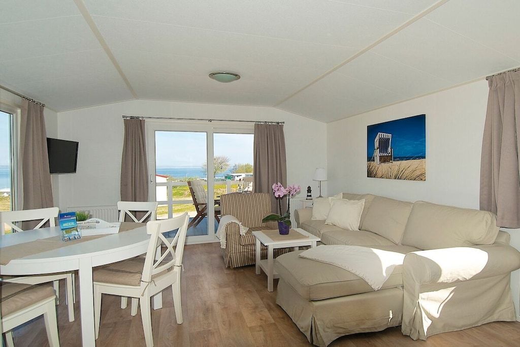 A furnished living room with a sofa, a dining table, and chairs, a television, and a view of the outdoors.