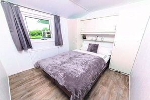 Ein Schlafzimmer mit einem Bett, einem Fenster mit Vorhängen, einem Heizkörper und einem weißen Kleiderschrank.