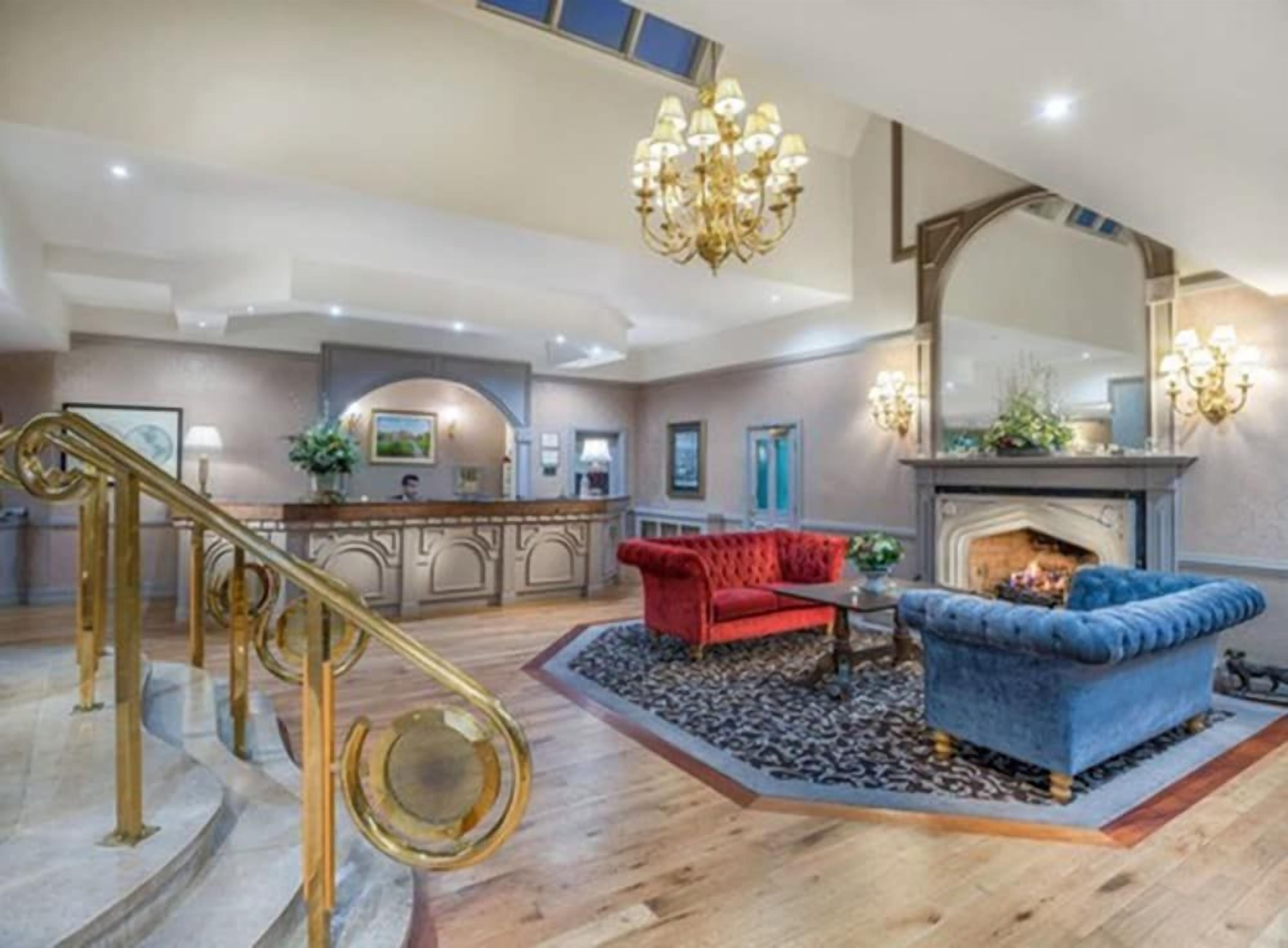 A spacious lobby with a grand staircase, a fireplace, and a seating area with red and blue upholstered sofas.